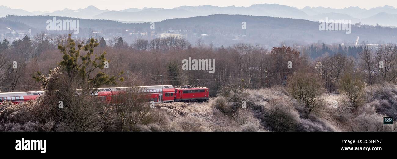 Rote Bahn durch oberbayerische Landschaft. Panorama mit Bäumen und Bergen (alpen) in der Ferne. Stockfoto