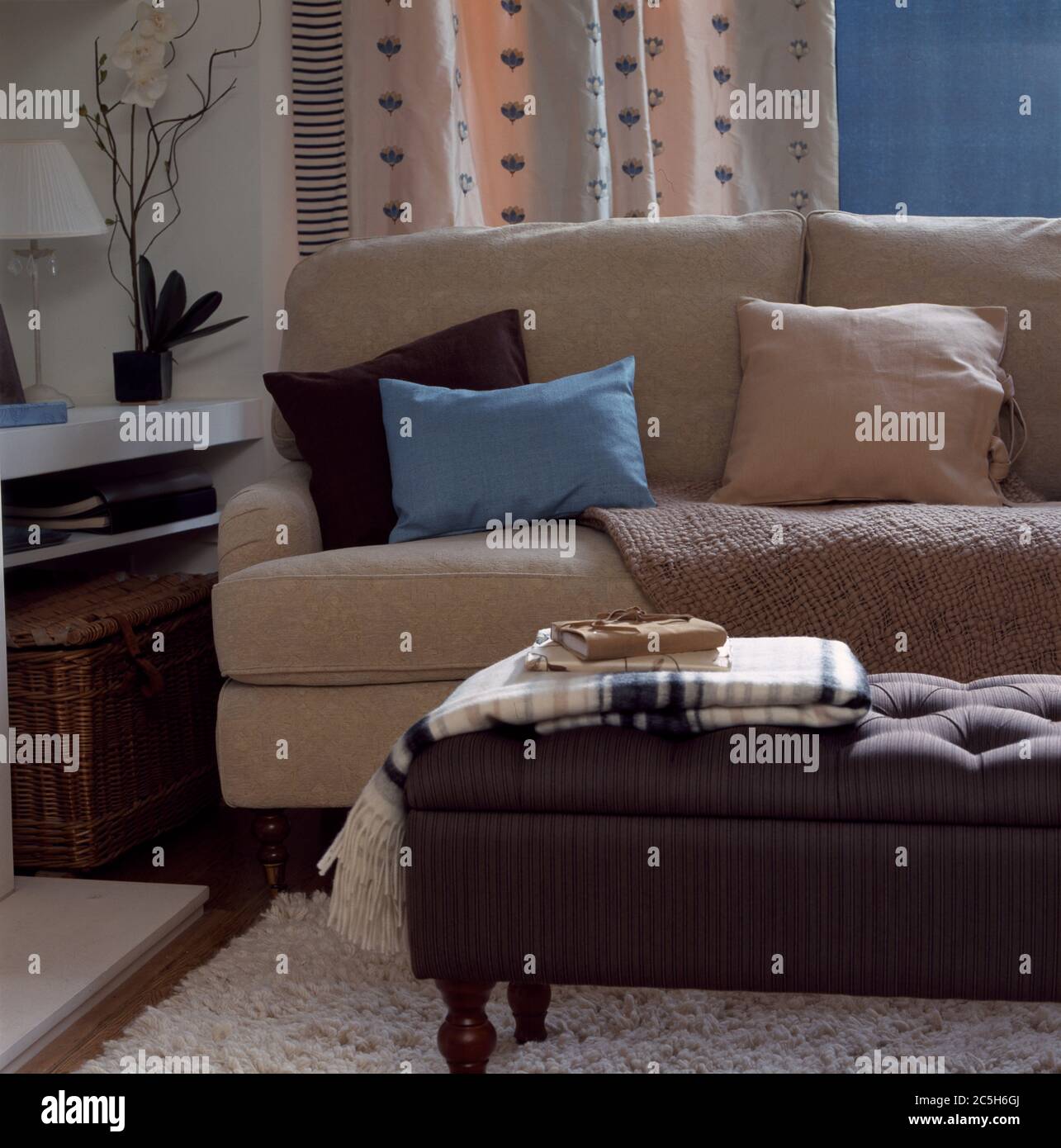 Bequemes beigefarbenes Sofa mit Fußhocker und Teppich Stockfoto