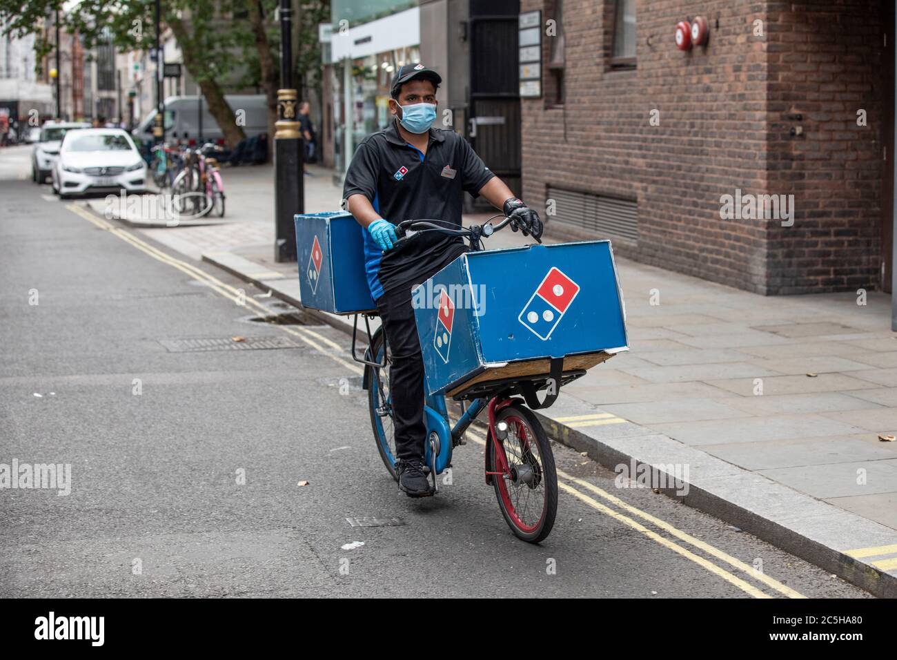 Domino's Pizza Lieferfahrradfahrer trägt Schutzmaske und Handschuhe während seiner Runde in Zentral-London, England, Großbritannien Stockfoto