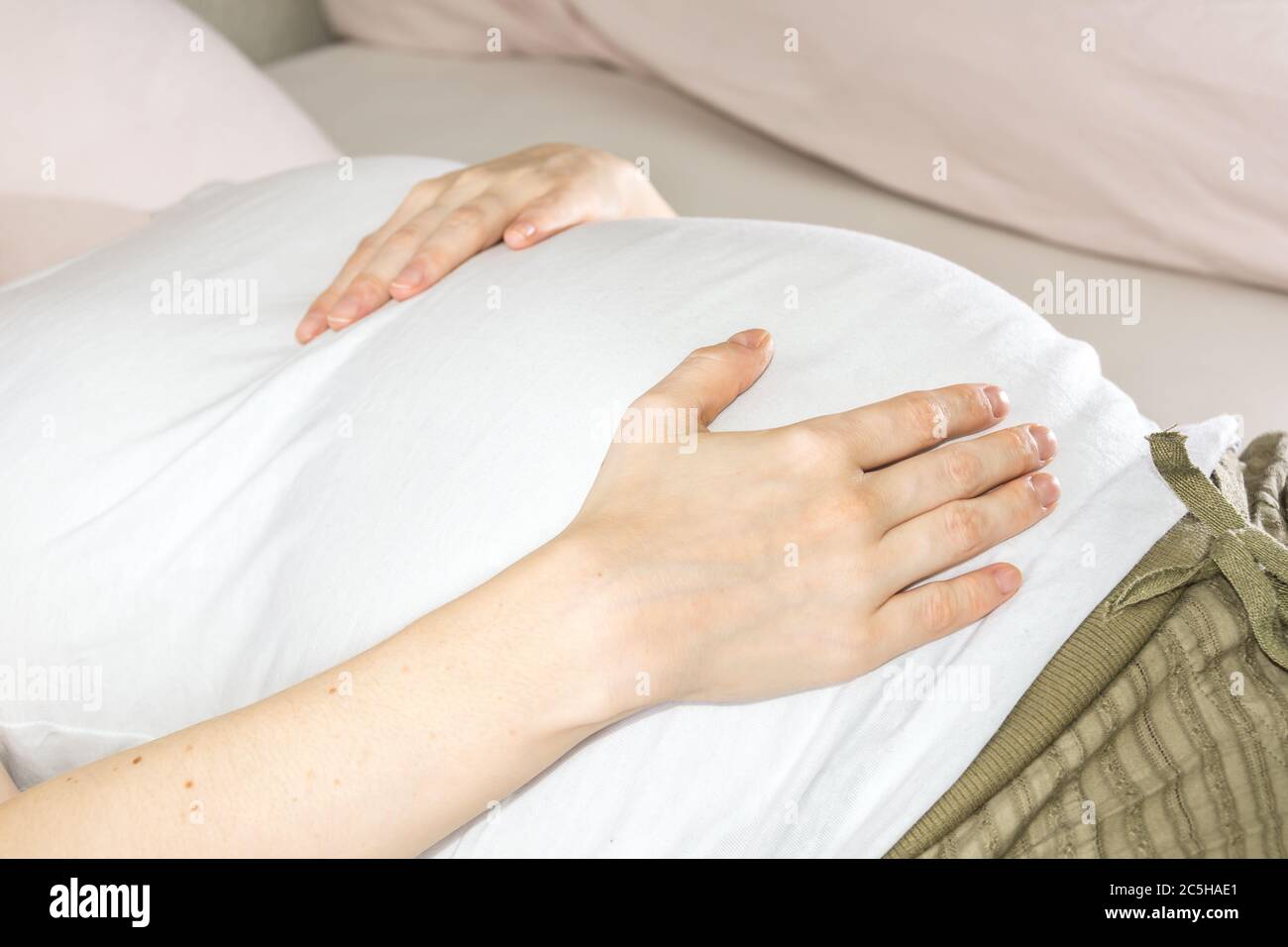 Nahaufnahme des Bauches der schwangeren Frau, während sie auf dem Bett liegt Stockfoto