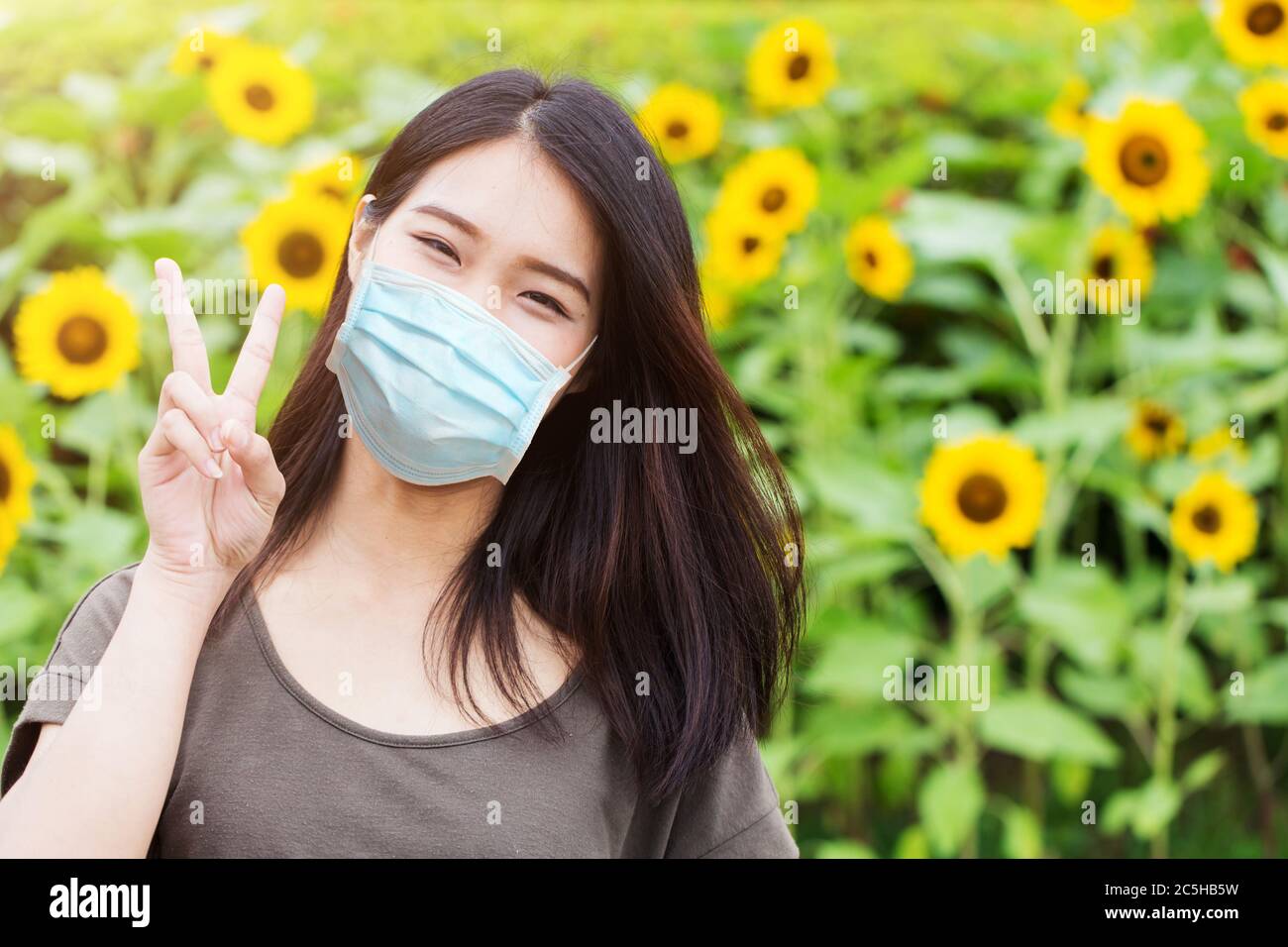 Nettes Mädchen Teen glücklich Ware Gesichtsmaske für Schutz Coronavirus (Covid-19) oder Luftverschmutzung oder Blütenpollen Allergie auf Sonnenblumen Park Hintergrund Stockfoto