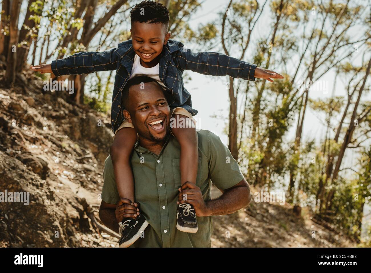 Mann, der seinen Sohn auf den Schultern trägt, während er auf einem Bergpfad geht. Vater und Sohn haben eine tolle Zeit zusammen in ihrem Urlaub. Stockfoto