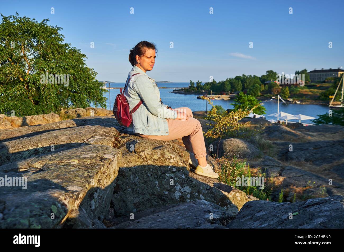 Die Frau sitzt auf dem Stein und blickt auf den Sonnenuntergang im Kaivopuisto Park, Helsinki, Finnland Stockfoto