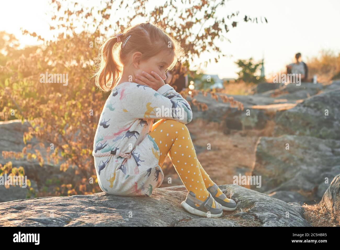 Trauriges Mädchen auf Steinen sitzend, Sonnenuntergang auf dem Hintergrund Stockfoto