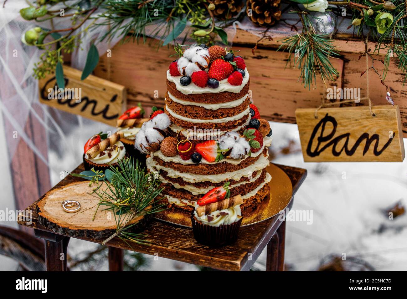 Hochzeitstorte mit Obst und einem alten Holztisch mit Dekorationen und Ringen während einer Hochzeitszeremonie im Winter auf Schnee inmitten einer Walddecke Stockfoto