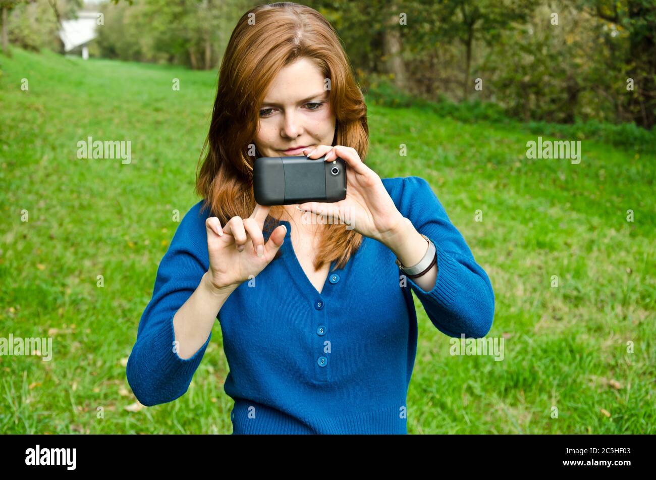 Junge Frau, die im Park mit ihrem Smartphone fotografiert Stockfoto