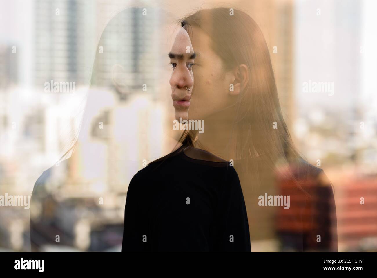 Junger asiatischer Mann mit langen Haaren in der Stadt mit mehrfacher Belichtung Stockfoto