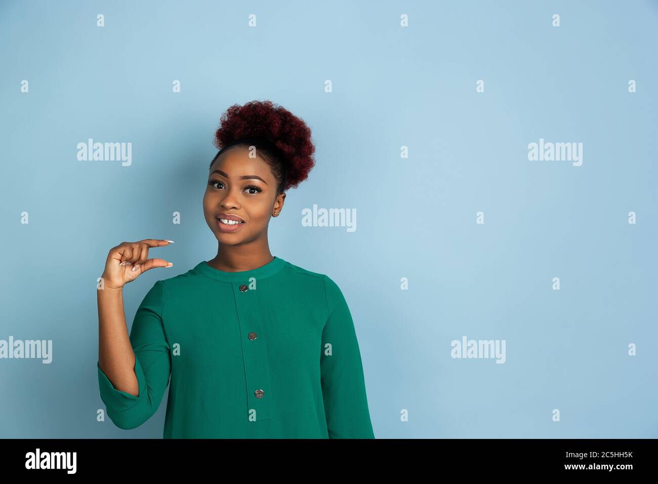 Etwas kleines zeigen. afroamerikanische junge Frau Porträt isoliert auf blauem Studio-Hintergrund. Schönes weibliches Modell. Konzept der menschlichen Emotionen, Gesichtsausdruck, Verkauf, Anzeige. Copyspace. Stockfoto
