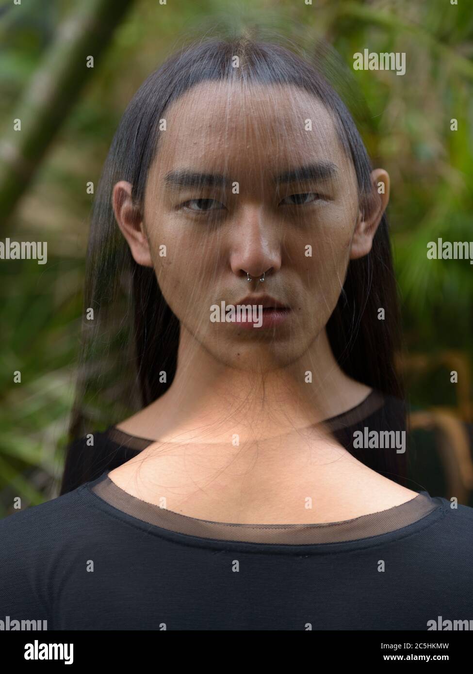 Junger asiatischer Mann mit langen Haaren im Park mit mehrfacher Belichtung Stockfoto