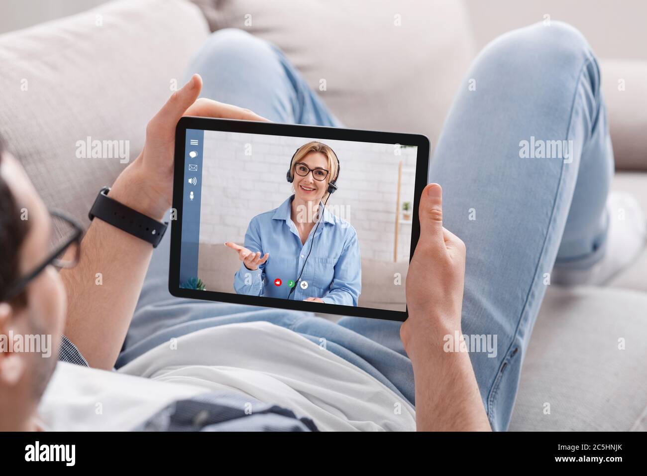 Online-Beratung. Kerl auf der Couch schaut auf Tablet auf Erwachsene Frau, kommuniziert mit ihm Stockfoto