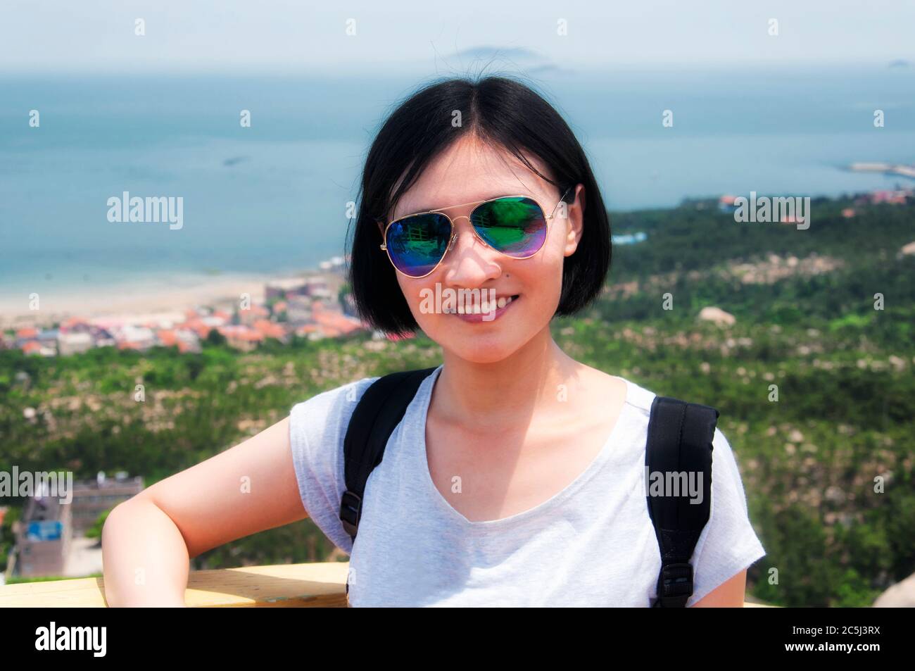 Eine lächelnde chinesin mit Sonnenbrille auf einem Aussichtspunkt auf dem Berg Lao mit dem ostchinesischen Meer im Hintergrund in Qingdao China shandong provin Stockfoto