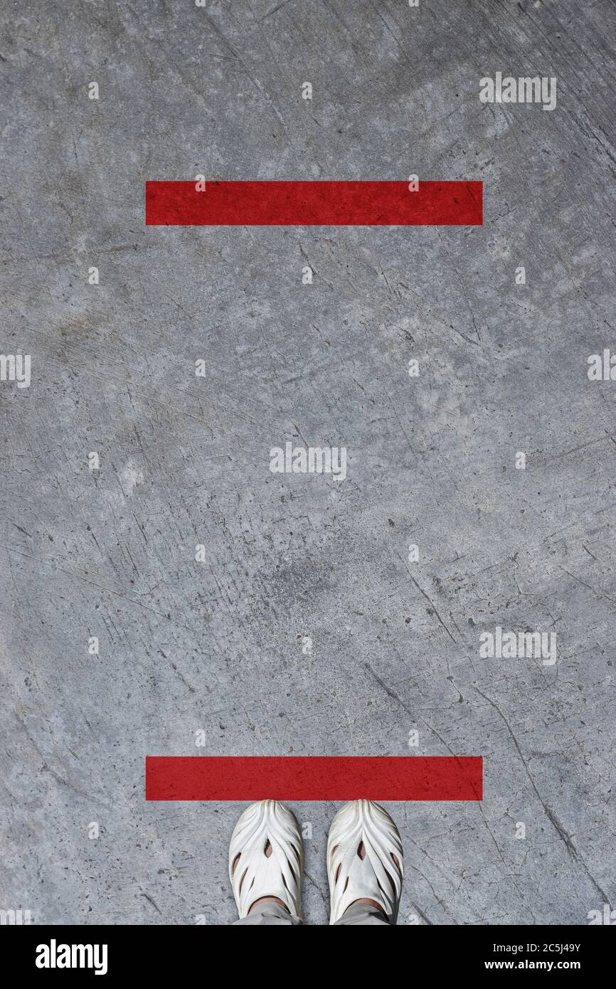 Die Füße stehen auf dem Boden gegen eine rote Linie. Konzept des öffentlichen Raums, der für soziale Distanzierung praktiziert. Stockfoto