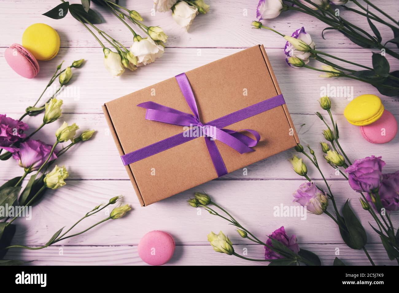 Geschenkbox mit Blumen und Makronen auf weißem Holzhintergrund. Grußkarte zum Geburtstag, Muttertag oder Valentinstag Stockfoto