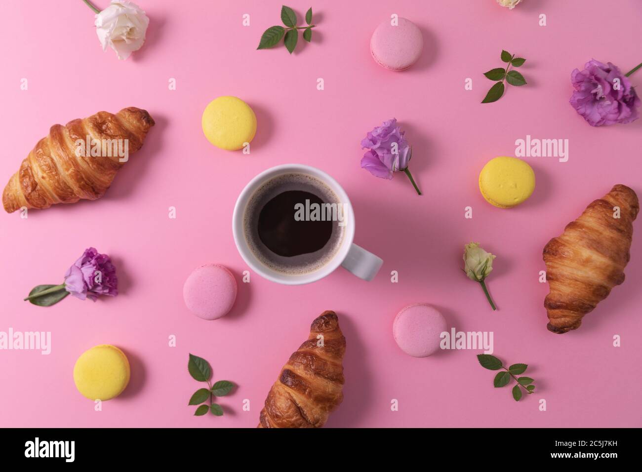 Croissants und Makronen mit Blumen und Tasse Kaffee auf rosa Hintergrund. Draufsicht Stockfoto