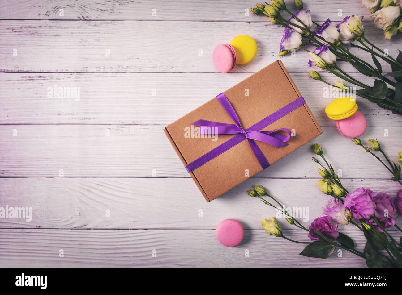 Geschenkbox mit Blumen und Makronen auf weißem Holzhintergrund mit Kopierraum. Grußkarte für Geburtstag, Muttertag oder Valentinstag Stockfoto