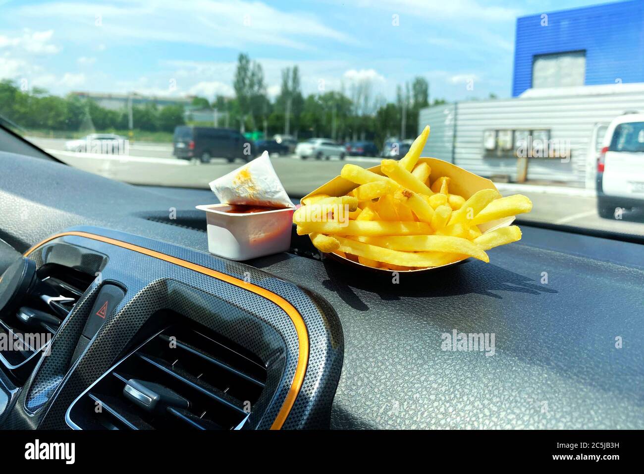 Pommes Frites und Ketchup zum Mittagessen. Snack auf der Konsole im Auto. Mittagspause auf der Fahrt mit dem Auto. Essen zum Mitnehmen, Street Food. Stockfoto