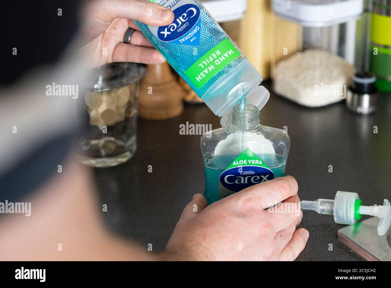 Hände eines Mannes, der einen Carex (Cussons) antibakterielle Flüssigseife hält, Handwaschdesinfektionsbehälter und diesen mit einer Nachfüllflasche auffüllt Stockfoto