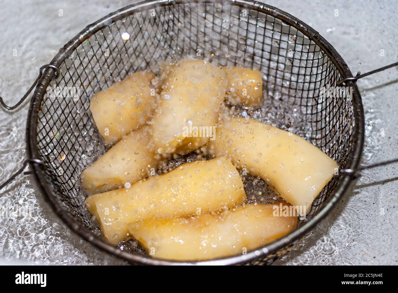 Waschen von Manihot mit Wasser in einem Metallsieb, Manihot esculenta. (Cassava roh Knolle). Maniok, auch Mandioca, Yuca, Balinghoy, mogo, Mantoca genannt Stockfoto