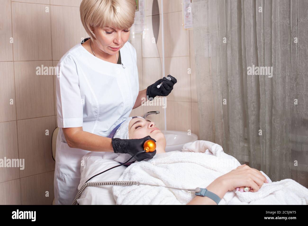 Die Kosmetikerin führt den Vorgang der Elektroporation im Schönheitssalon durch. Die Einführung von Nährstoffen in die Dermis aufgrund der niedrigen Frequenz c Stockfoto