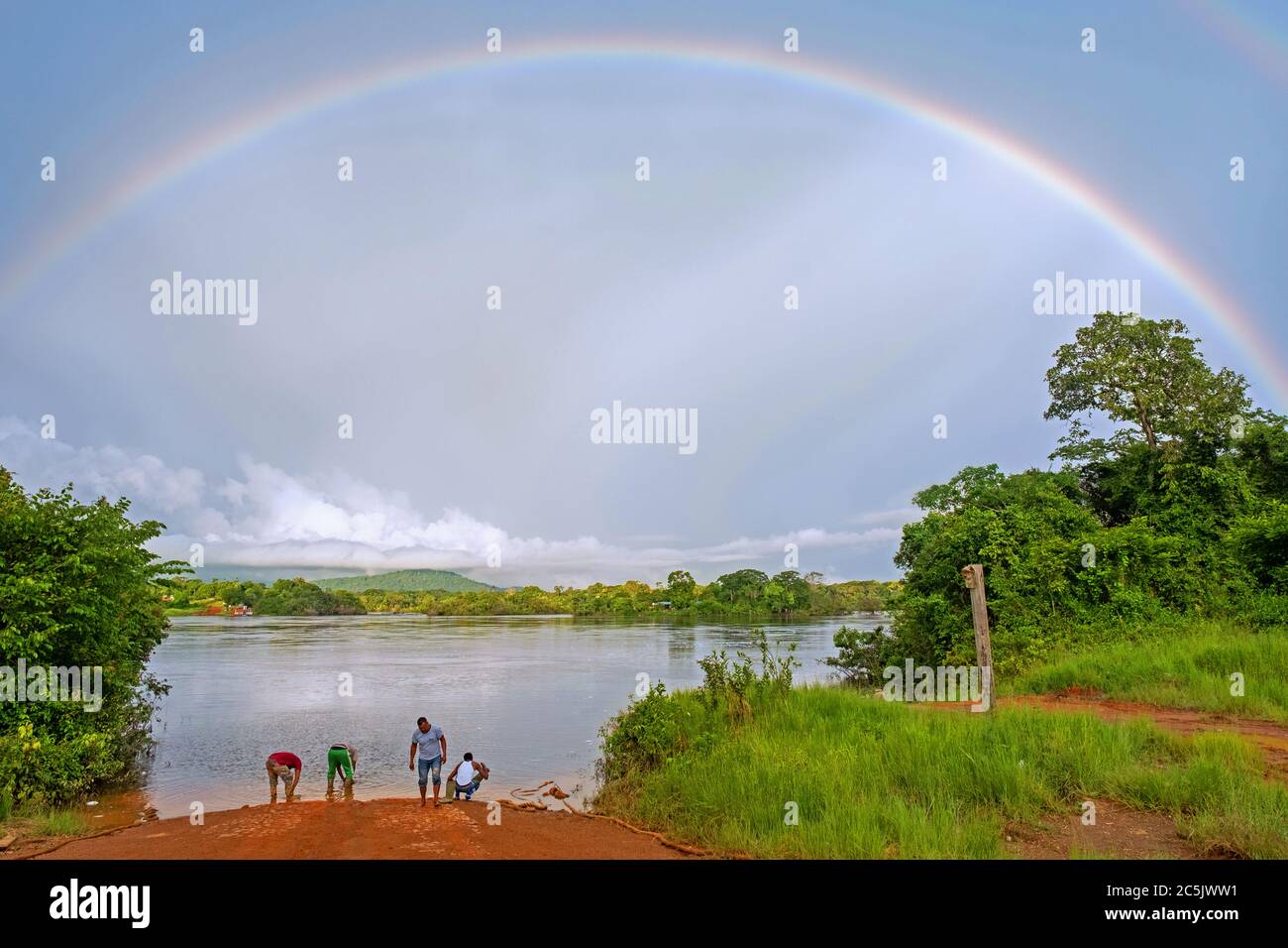 Regenbogen und Einheimische warten auf Fähre auf dem Essequibo Fluss in der Regenzeit entlang der Linden-Lethem Schotterstraße, Guyana, Südamerika Stockfoto