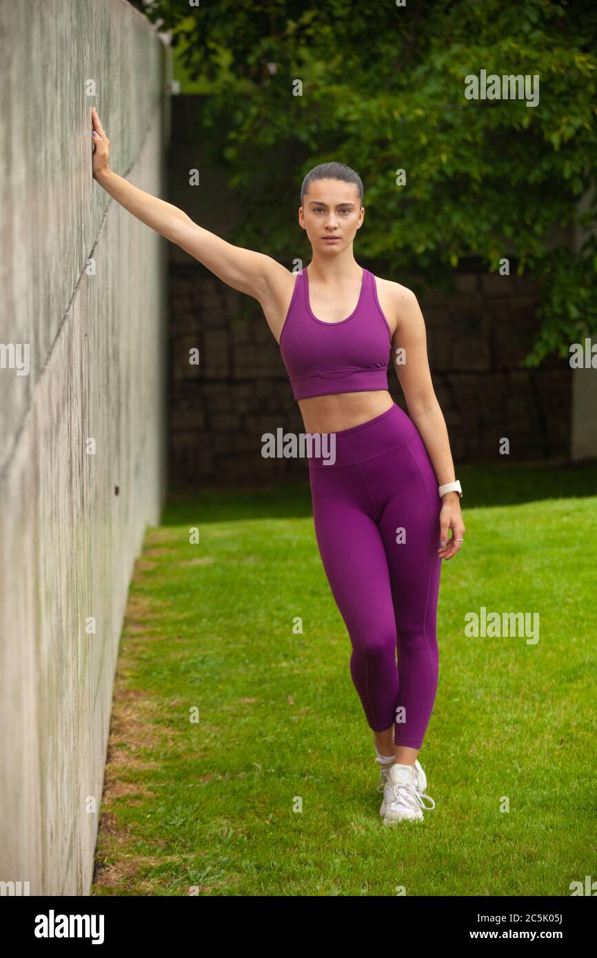 Eine attraktive Frau, die Sportkleidung trägt und sich draußen an einer Betonwand lehnt. Stockfoto