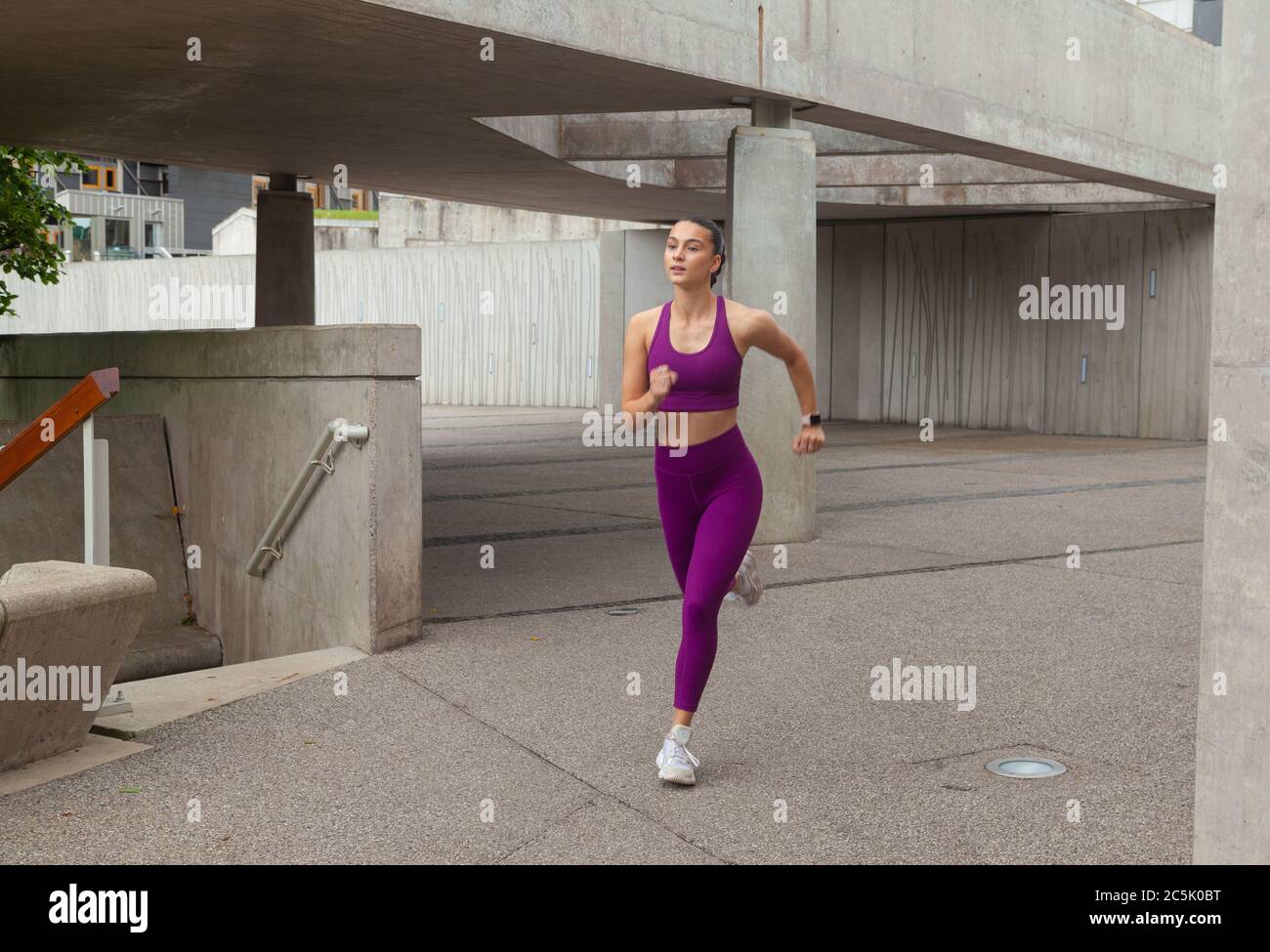 Eine attraktive Frau in Sportkleidung, die durch eine konkrete Stadtumgebung läuft. Stockfoto