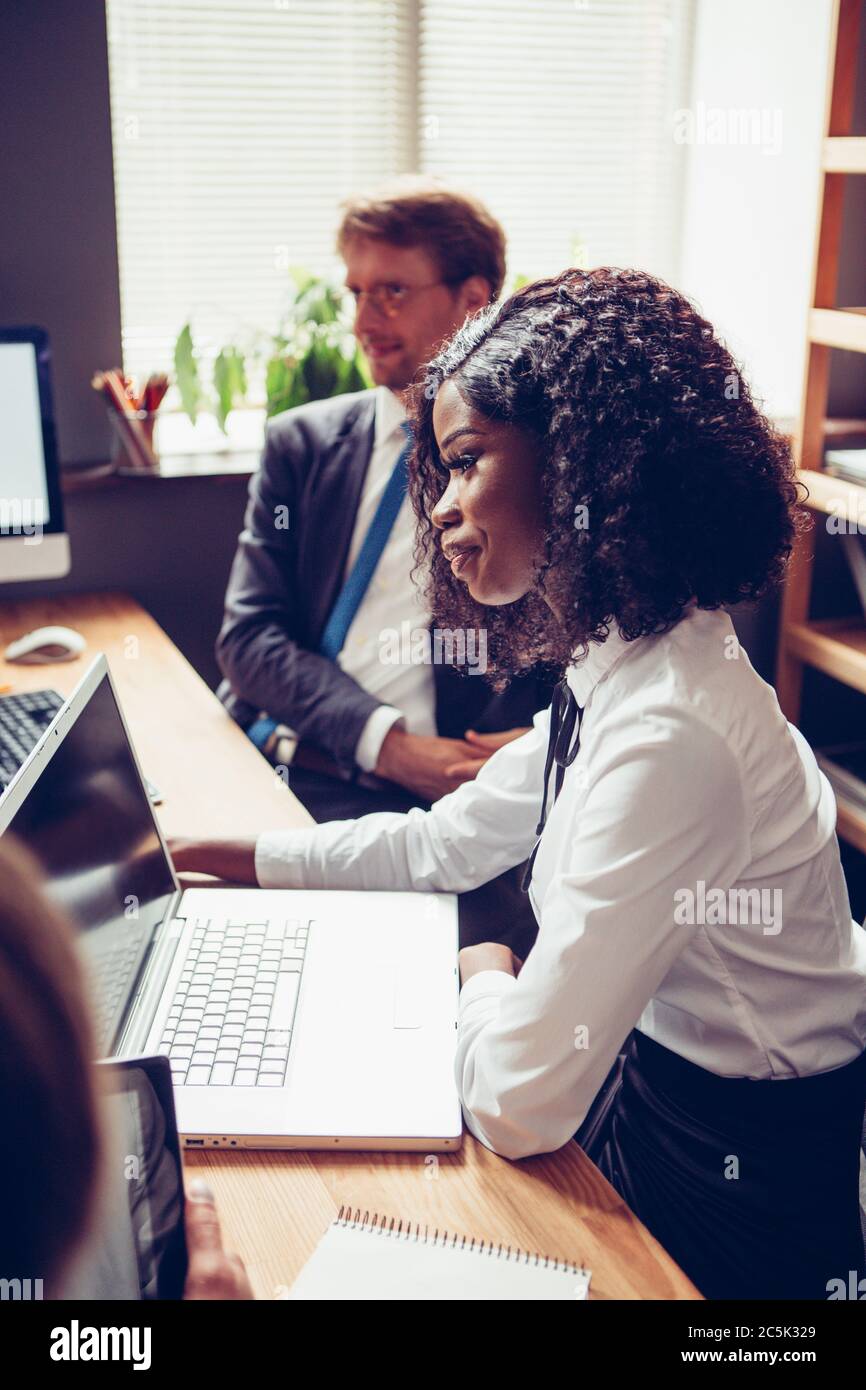 Seitenansicht einer afroamerikanischen jungen Frau, die mit ihren Kollegen am Tisch sitzt. Teamarbeit in einer vielfältigen Gruppe. Getöntes Bild Stockfoto