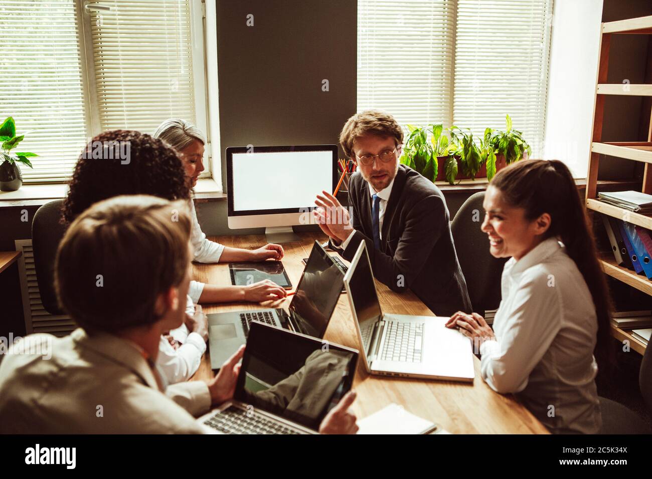 Teamarbeit von verschiedenen Gruppen, die am Verhandlungstisch mit Computern darauf sitzen. Diskussion oder Brainstorming von Geschäftsleuten in modernen Büros. Getönte Stockfoto