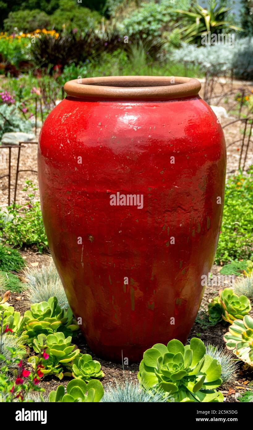 Leuchtend rote, große dekorative Keramik-Glas ist ein Schwerpunkt in einem Garten Blumenbeet. Wohnkultur Idee für Gartendekoration. Stockfoto