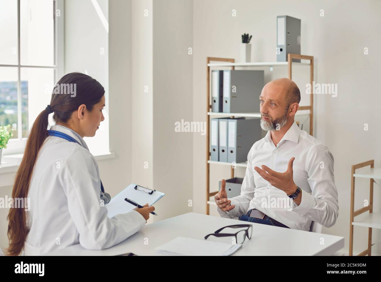 Der Rentner spricht mit dem Arzt am Schreibtisch im Büro des Krankenhauses. Der Arzt diagnostiziert die Symptome der Erkrankung im Pat Stockfoto