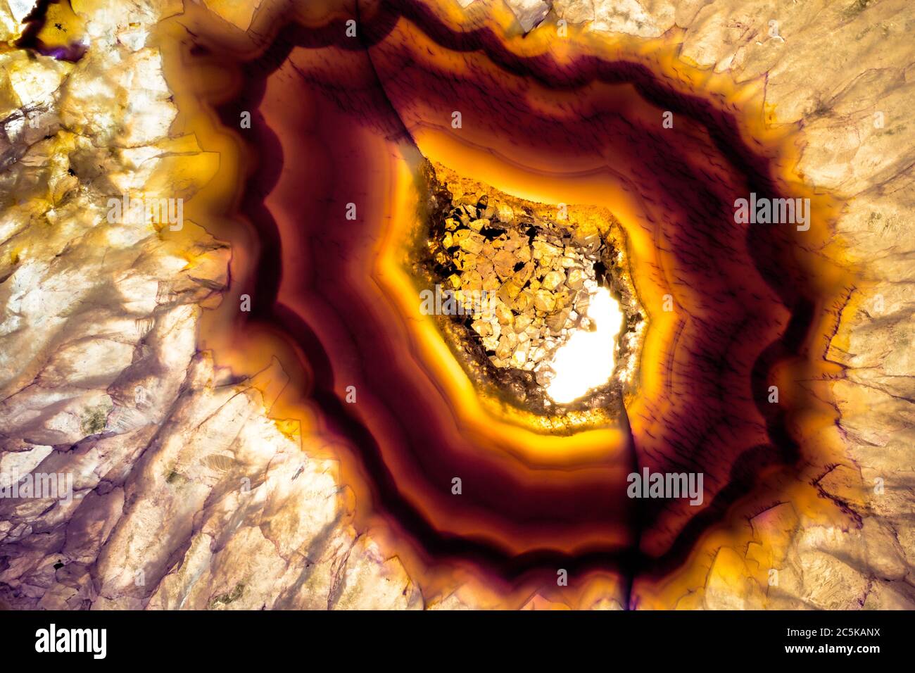 Makrofoto einer bunten violetten und gelben Achatscheibe. Ich beleuchtete es von unten, um die mineralischen Texturen und Kristallfarben herauszubringen. Stockfoto