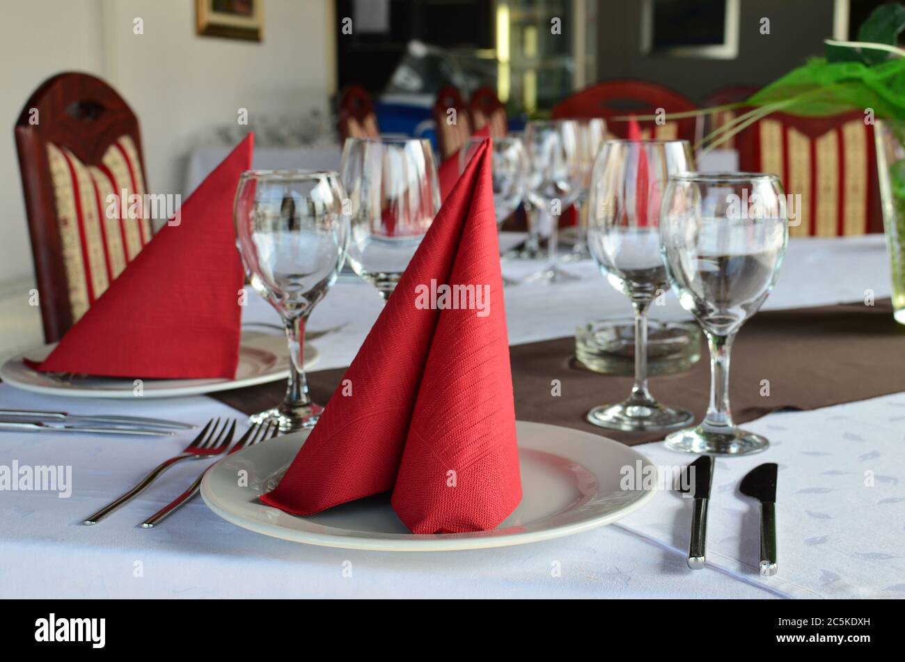Restauranttisch gelegt und dekoriert, leere Gläser, Teller, Gabeln und Messer, rote Servietten und weiße Tischtücher Stockfoto