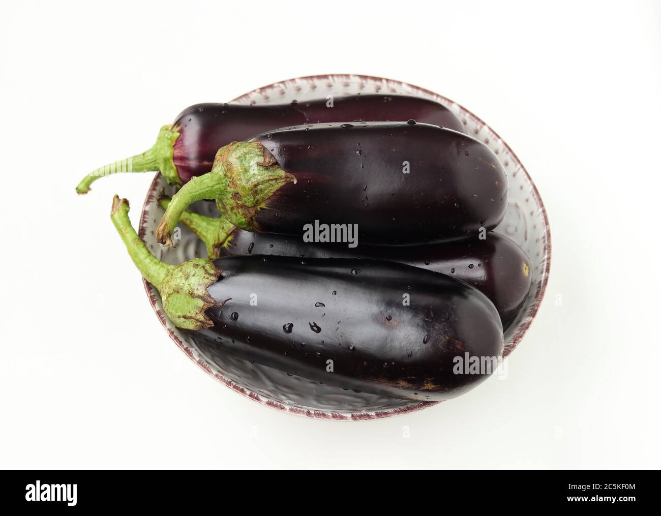 Vier große Auberginen mit Wassertropfen auf einem Teller, weißer Hintergrund, Bio-Food-Konzept, Nahaufnahme, Draufsicht Stockfoto