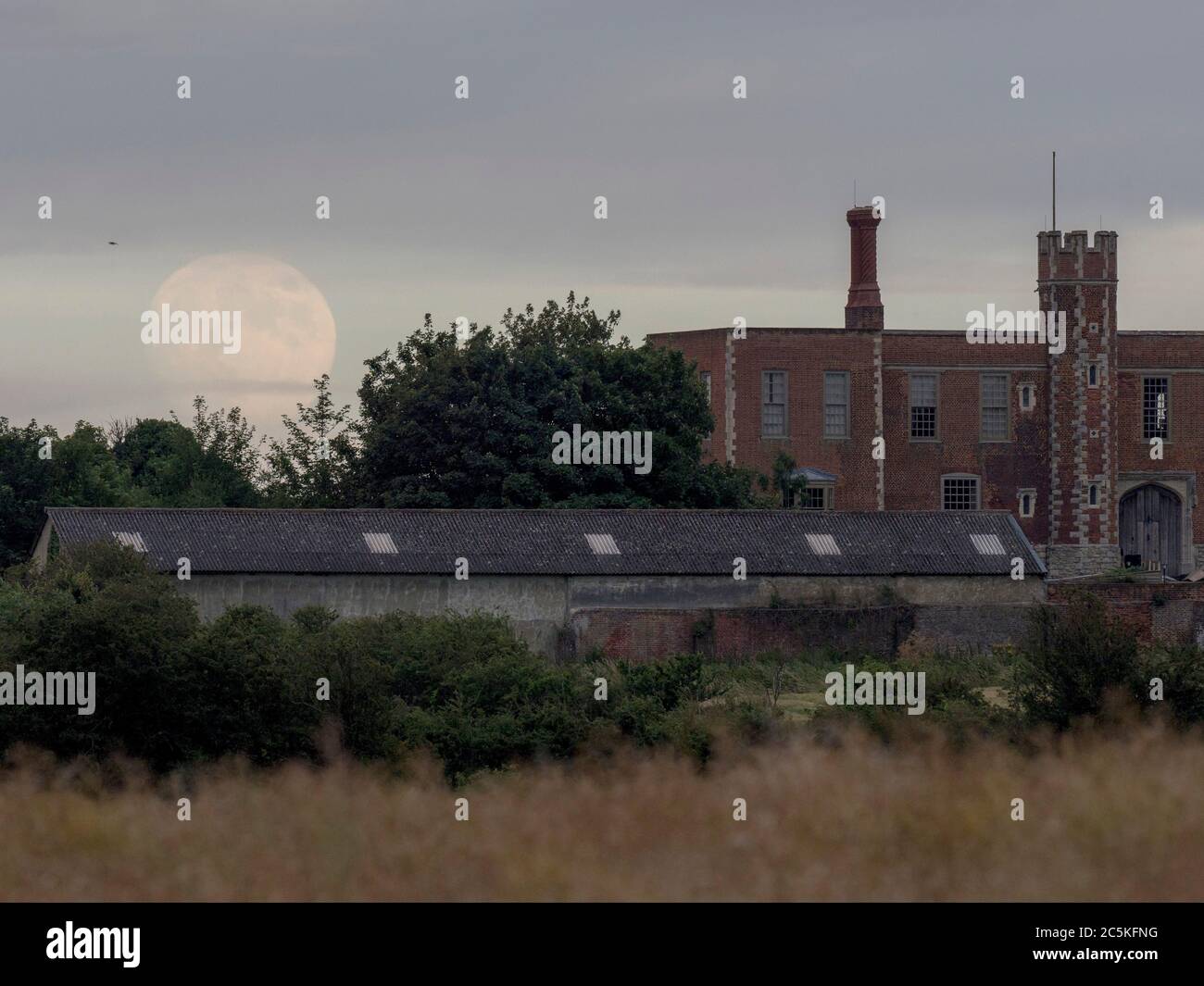 Eastchurch, Kent, Großbritannien. Juli 2020. UK Wetter: Der fast Vollmond, der über Shurland Hall in Eastchurch, Kent durch eine Lücke in schwerer Wolkendecke aufsteigt. Der Vollmond des Juli ist als Buck- oder Thunder-Mond bekannt. Quelle: James Bell/Alamy Live News Stockfoto