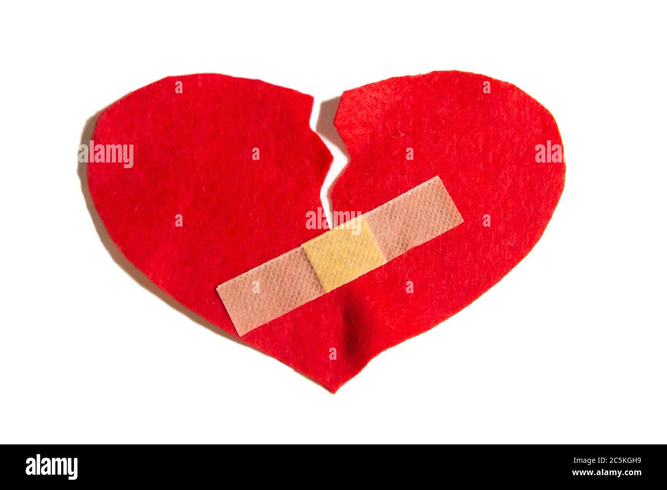 Gebrochenes Herz und mit einem Pfand zusammengeklebt. Ein Herz aus Filz. Ein Konzept über gebrochene Liebe. Herz mit Gips isoliert auf weißem Hintergrund Stockfoto
