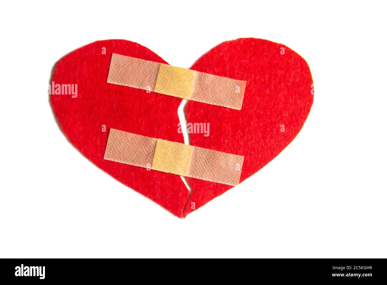 Gebrochenes Herz und mit einem Pfand zusammengeklebt. Ein Herz aus Filz. Ein Konzept über gebrochene Liebe. Herz mit Gips isoliert auf weißem Hintergrund Stockfoto