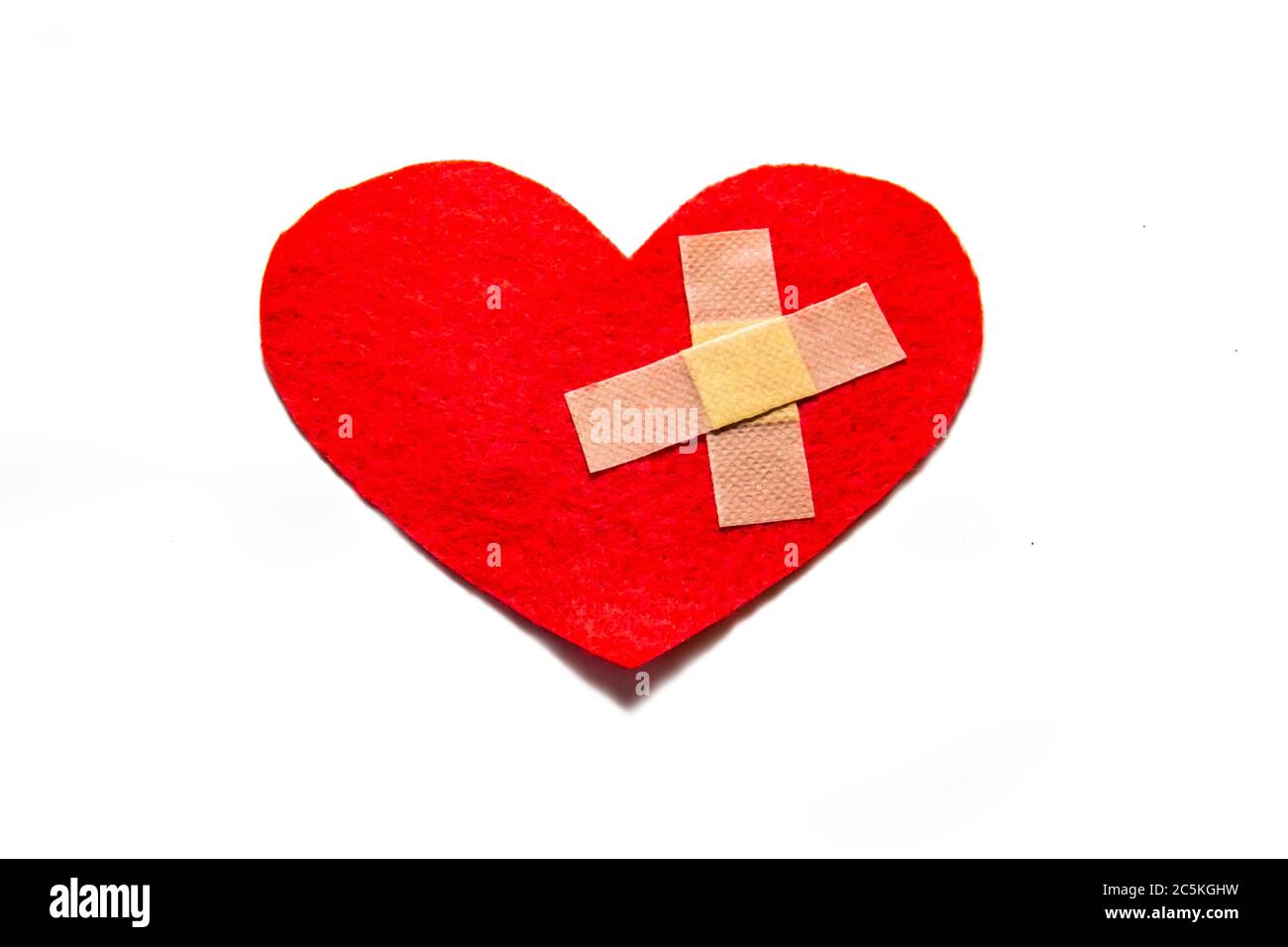 Gebrochenes Herz und mit einem Pfand zusammengeklebt. Ein Herz aus Filz. Ein Konzept über gebrochene Liebe. Herz mit Gips isoliert auf weißem Hintergrund Stockfoto