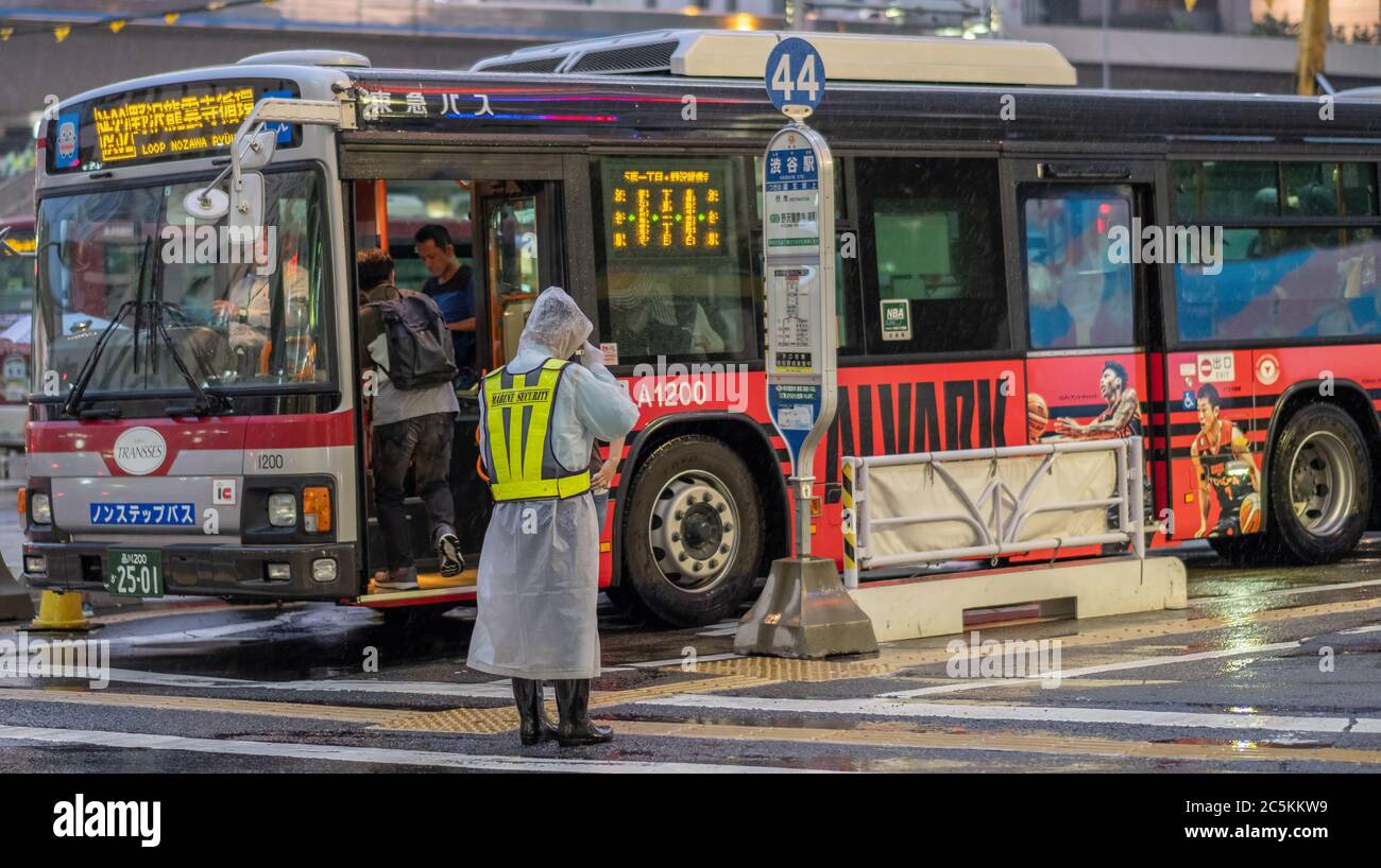 Verkehrsführer, der in der Straße von Shibuya in einer regnerischen Nacht arbeitet, Tokyo, Japan Stockfoto