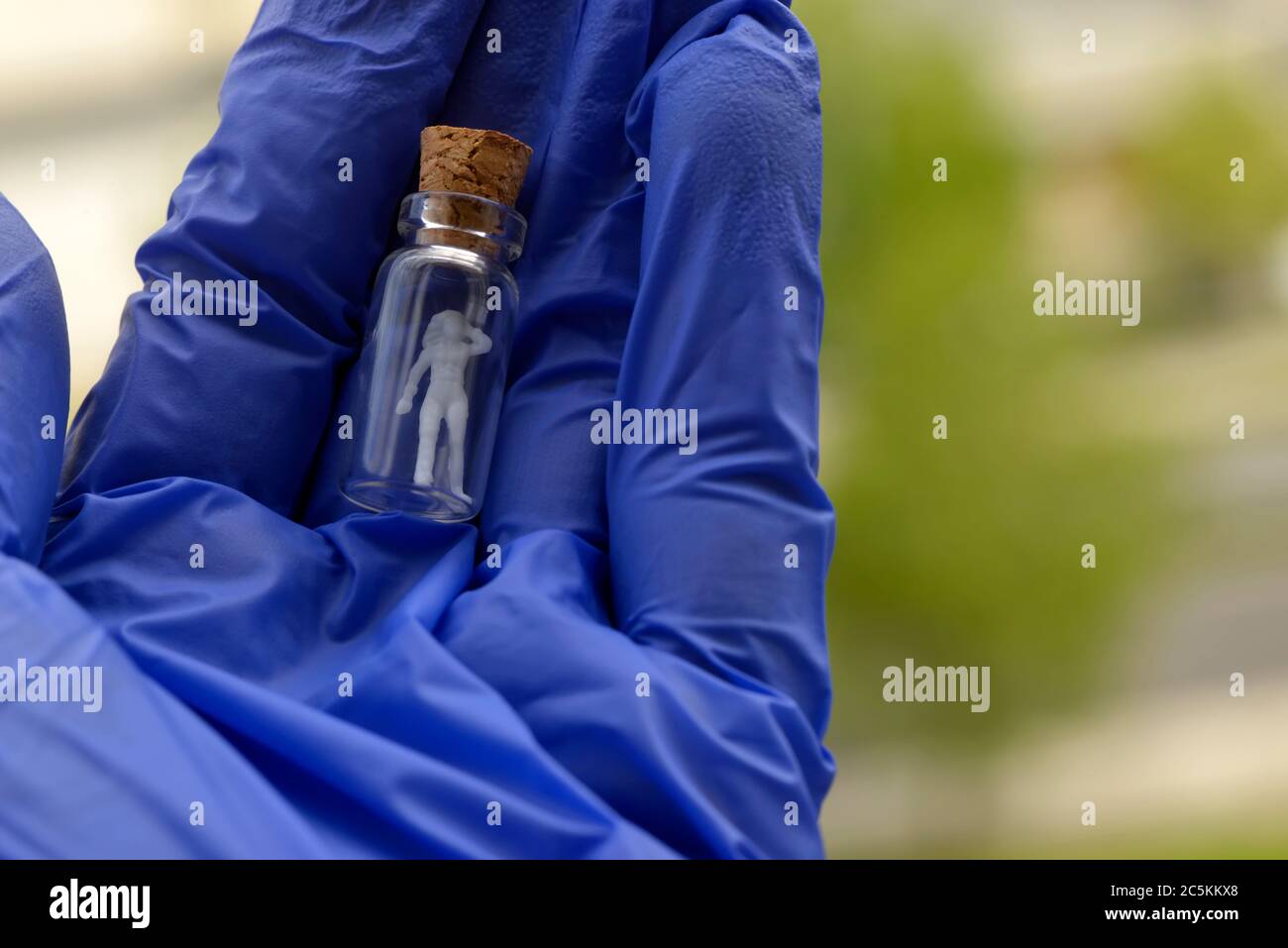 Covid-19, Schutz gefährdeter Menschen vor Coronavirus, Konzept. Figur einer Frau Person in einer Glasflasche auf einer Hand mit Einweghandschuh Stockfoto