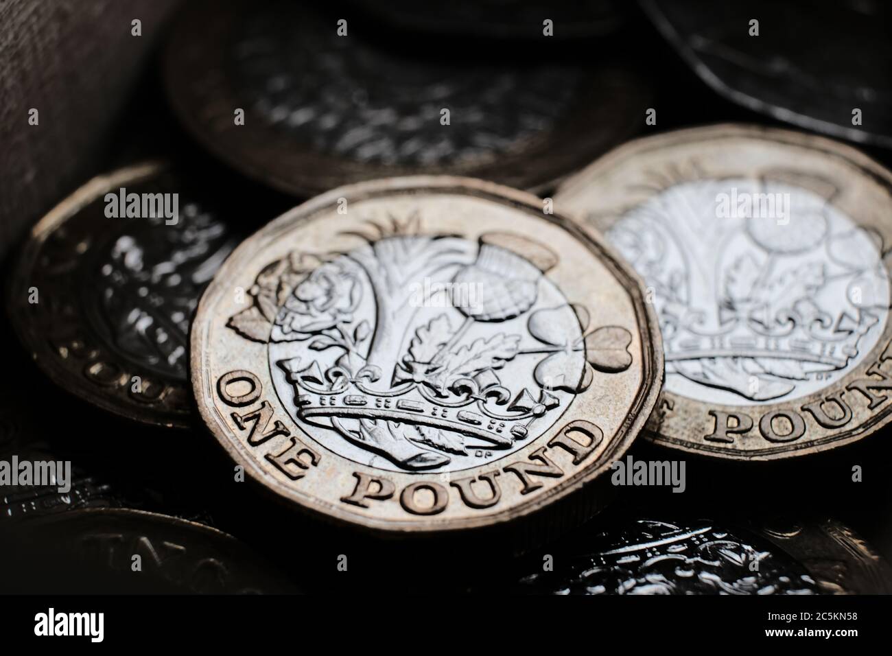 Britische 1-Pfund-Münzen, die in der Box übereinander gelegt werden. Makrofoto mit dramatischen Schatten. Stockfoto