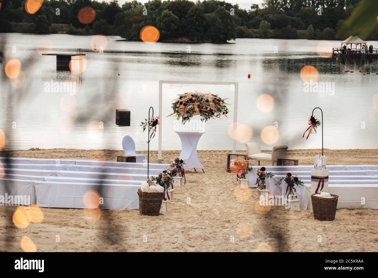 Hochzeitsdekoration - weiße Bänke mit Stoffbehang und Blumendekoration am Sandstrand. Draußen Nuptials. Hochzeitskonzept. Stockfoto