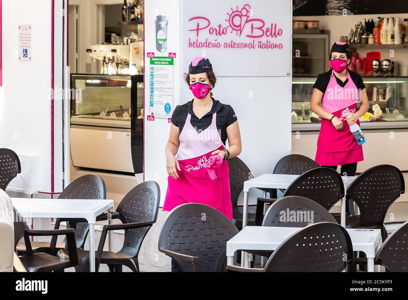Punta Umbria, Huelva, Spanien - 3. Juni 2020: Eine Kellnerin in einer Schutzmaske wird die Tische der Porto Bello Eisdiele in Th reinigen Stockfoto