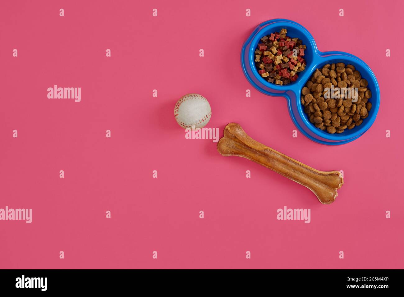 Trockenes Tierfutter in Schale mit einem Ball und Hundeknochen auf rosa Hintergrund Draufsicht Stockfoto