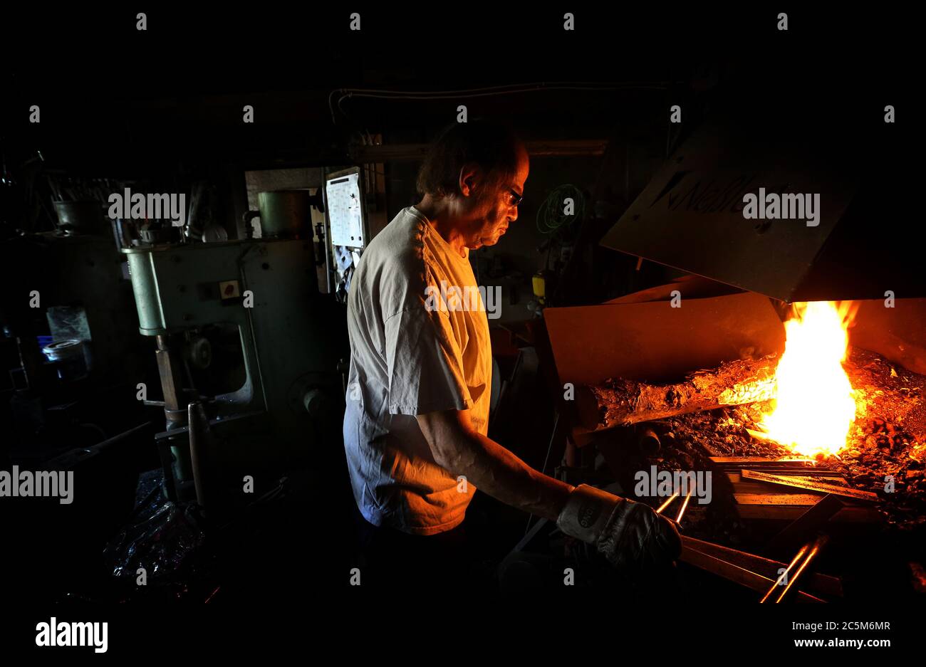 Bad Hindelang, Deutschland. Juli 2020. Konrad Neßler steht in seiner  Schmiede an einem Kamin, in dem er Stahlstäbe erwärmt, um daraus dann  Pfannengriffe zu Formen. Der 57-jährige Schmied arbeitet in seiner Werkstatt