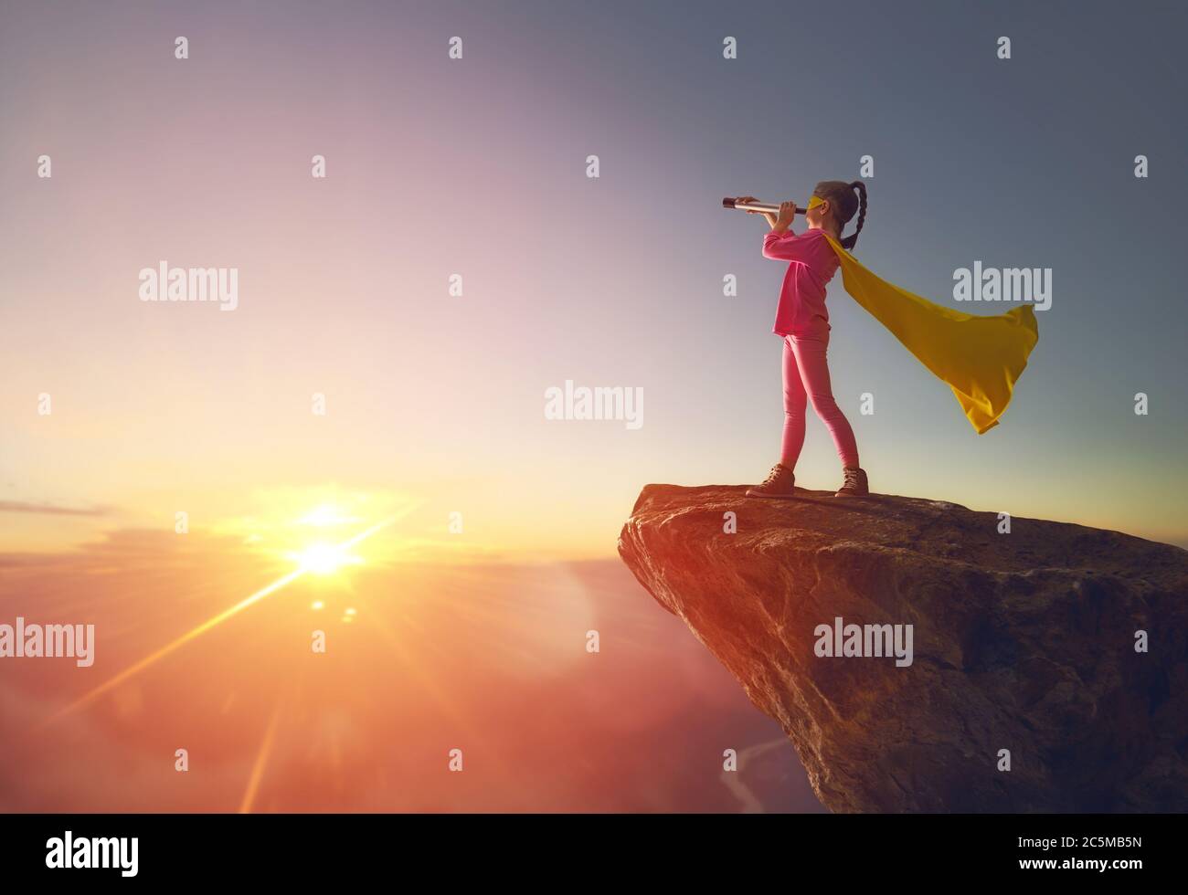 Kleines Kind Mädchen ist Superheld spielen. Kind auf dem Hintergrund des Sonnenuntergangs Himmel. Mädchen Power Konzept Stockfoto