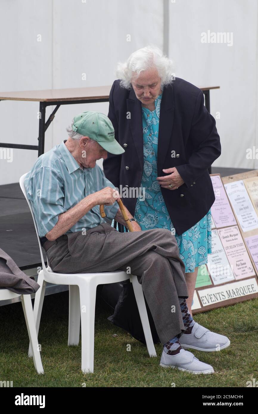 Ältere Paare, die sich auf einer Messe in london unterhalten. Sie steht und er sitzt auf einem Stuhl Stockfoto