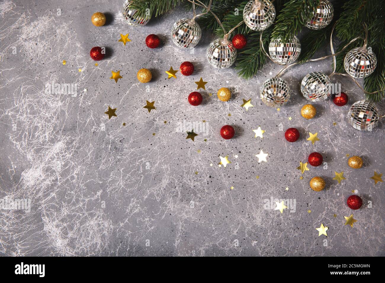 Weihnachtsbaum Zweig mit dekorativen Girlanden Kugeln glühendes Licht auf grauem Hintergrund mit goldenen und roten Kugeln und Sternen Stockfoto