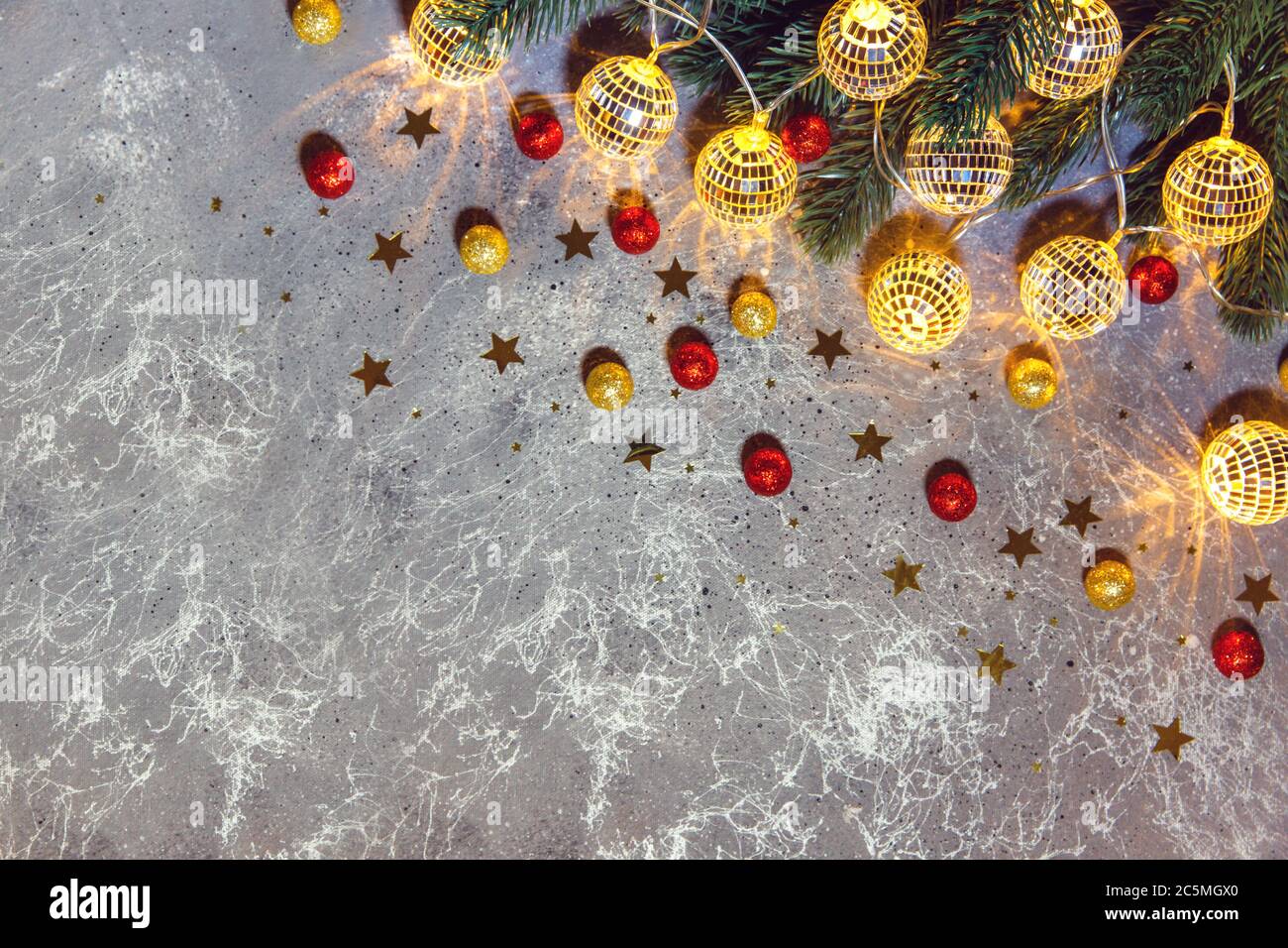 Weihnachtsbaum Zweig mit dekorativen Girlanden Kugeln glühendes Licht auf grauem Hintergrund mit goldenen und roten Kugeln und Sternen Stockfoto