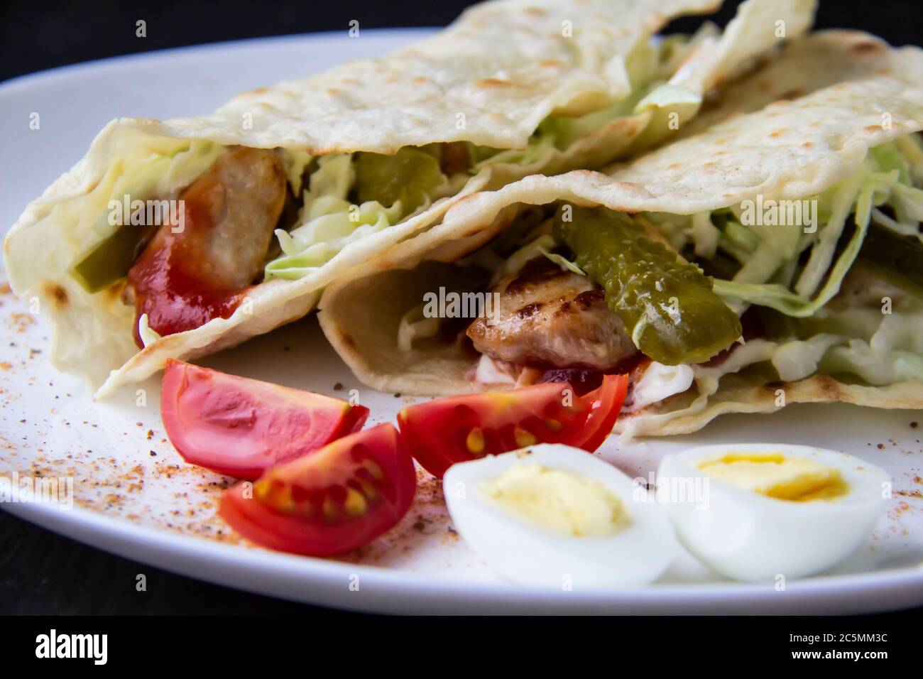 ​​chicken in Scheiben geschnitten mit Gurken aus der Dose und Kohl in Sauce, in Pita-Brot auf einem weißen Teller eingewickelt. Köstlich zum Mittag- oder Abendessen. Tomatenstücke Stockfoto