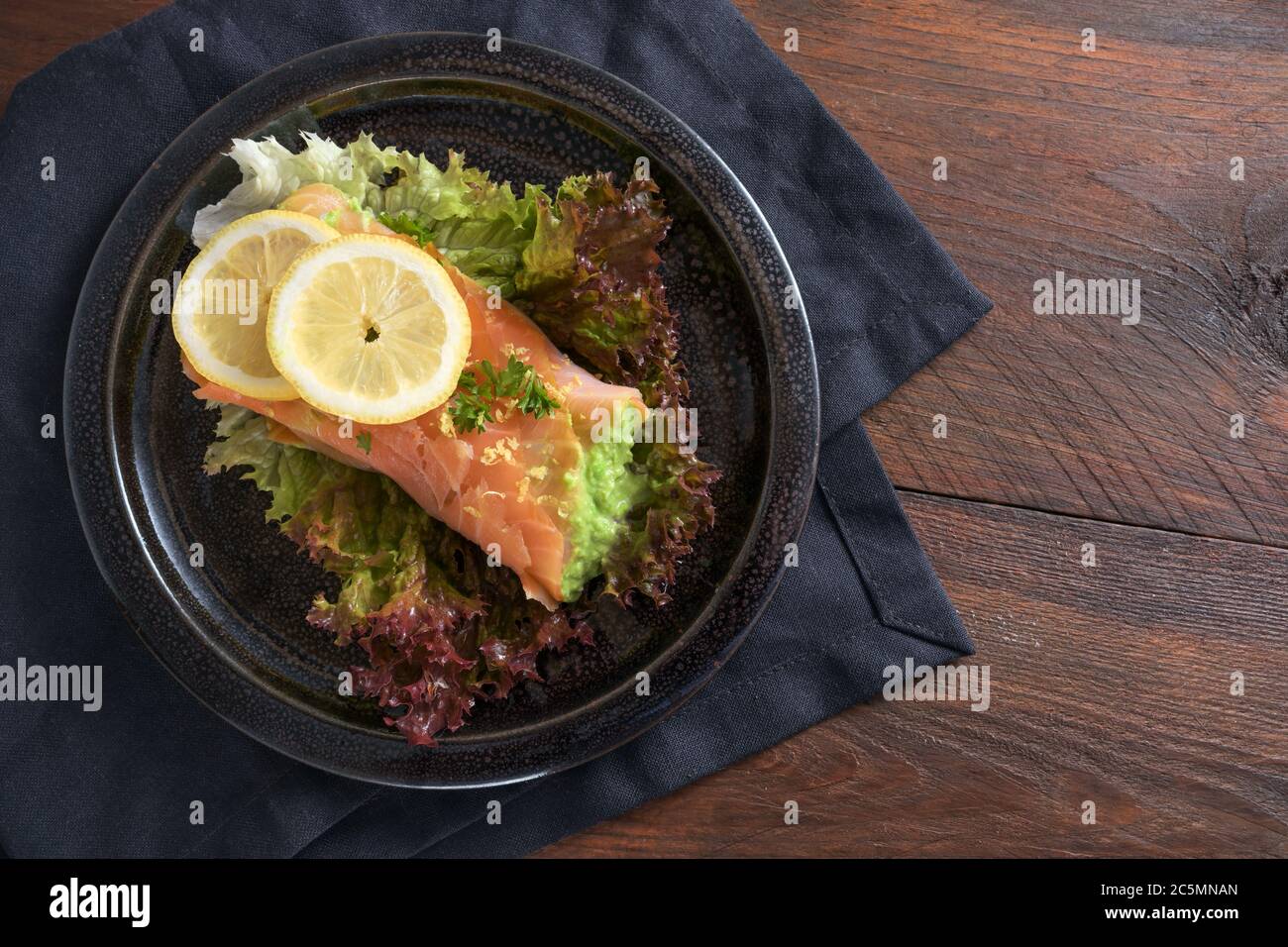 Kohlenhydratarme oder ketogene Ernährung, geräuchertes Lachsrollen gefüllt mit Erbsenpüree auf Salat mit Zitronenscheiben und Petersilie garnieren auf einem dunklen Teller und Serviette Stockfoto